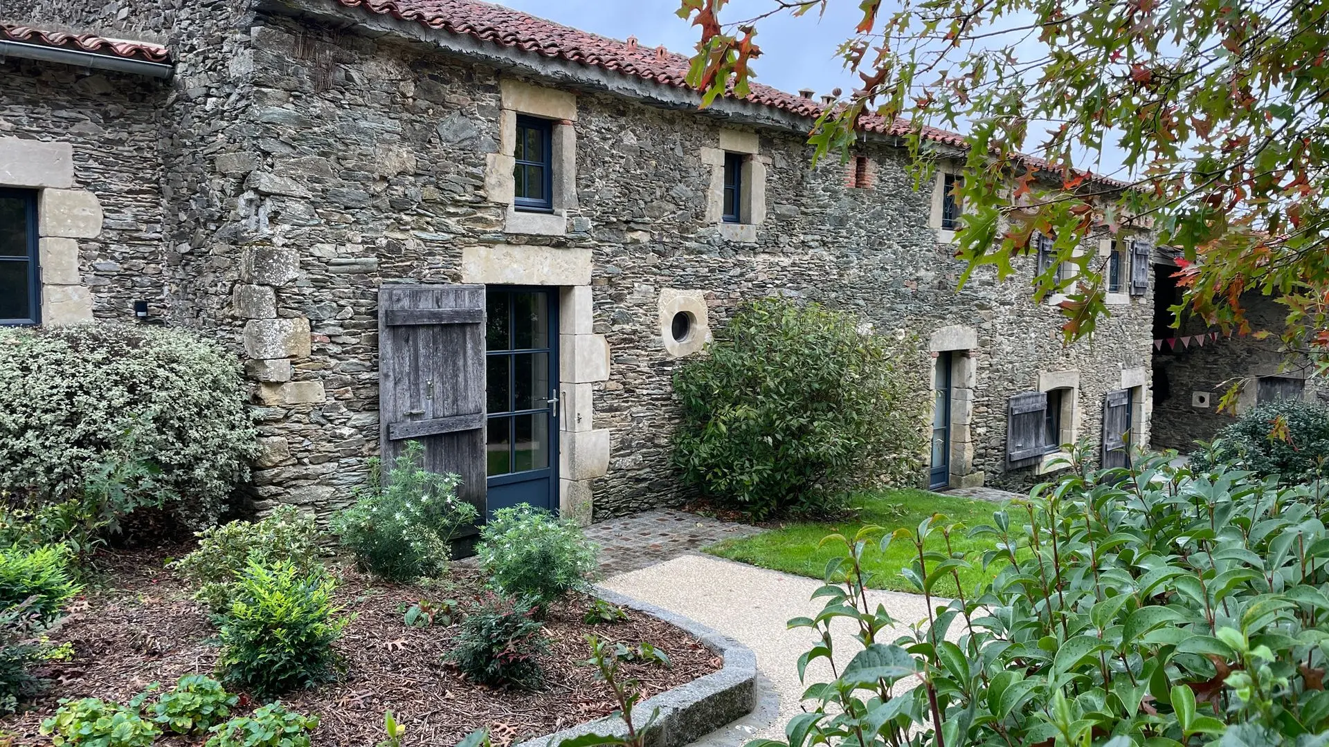 Façade en pierre du gîte Alexandrin avec volets en bois, allée de gravier et jardin, à La Bréjolière